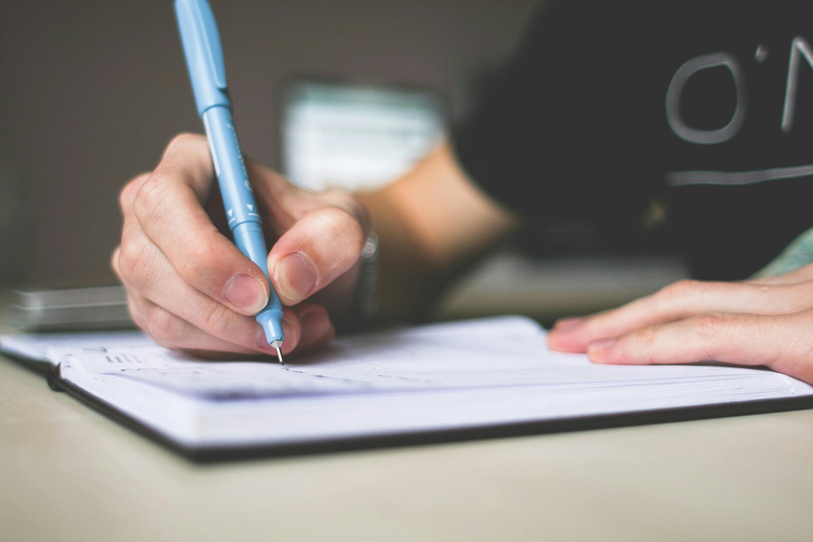 Close-up of hand writing in notebook using a blue pen, focus on creativity.